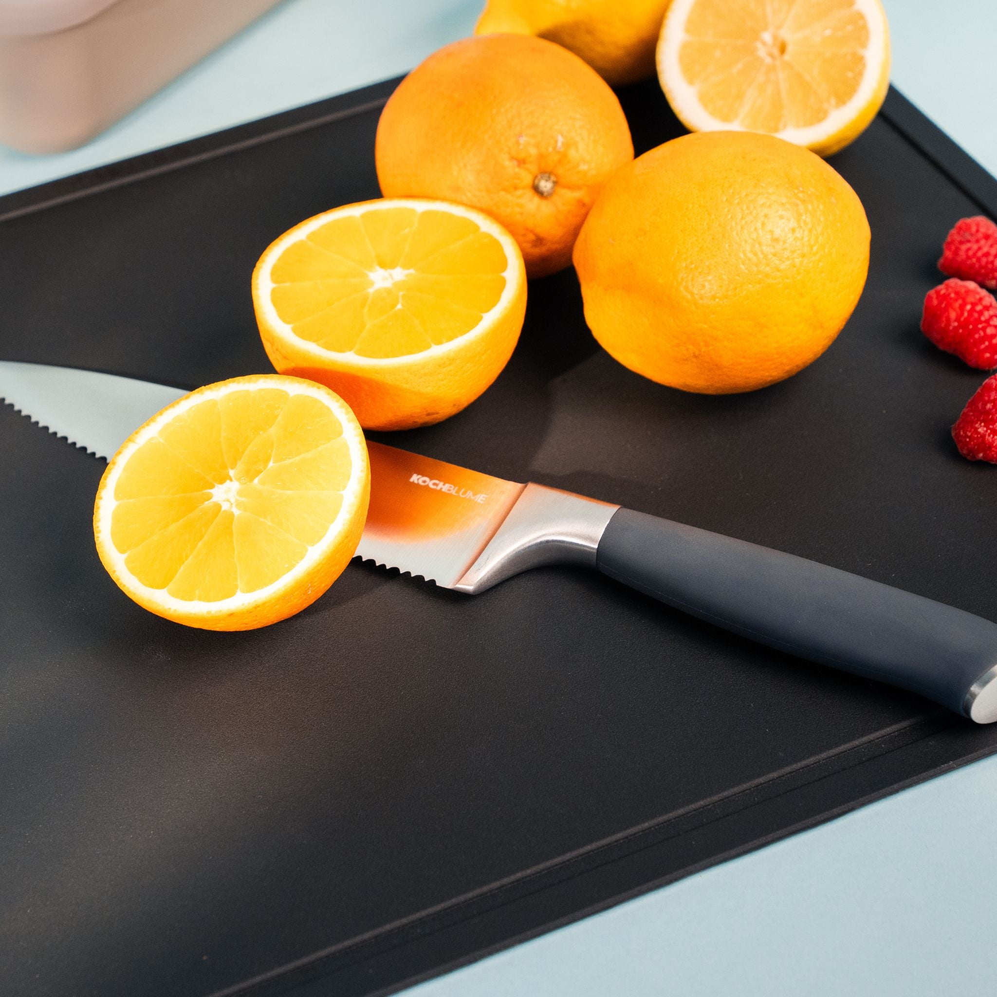 Schwarze Schneidunterlage mit aufgeschnittenen Orangen und einem Messer mit schwarzem Griff.