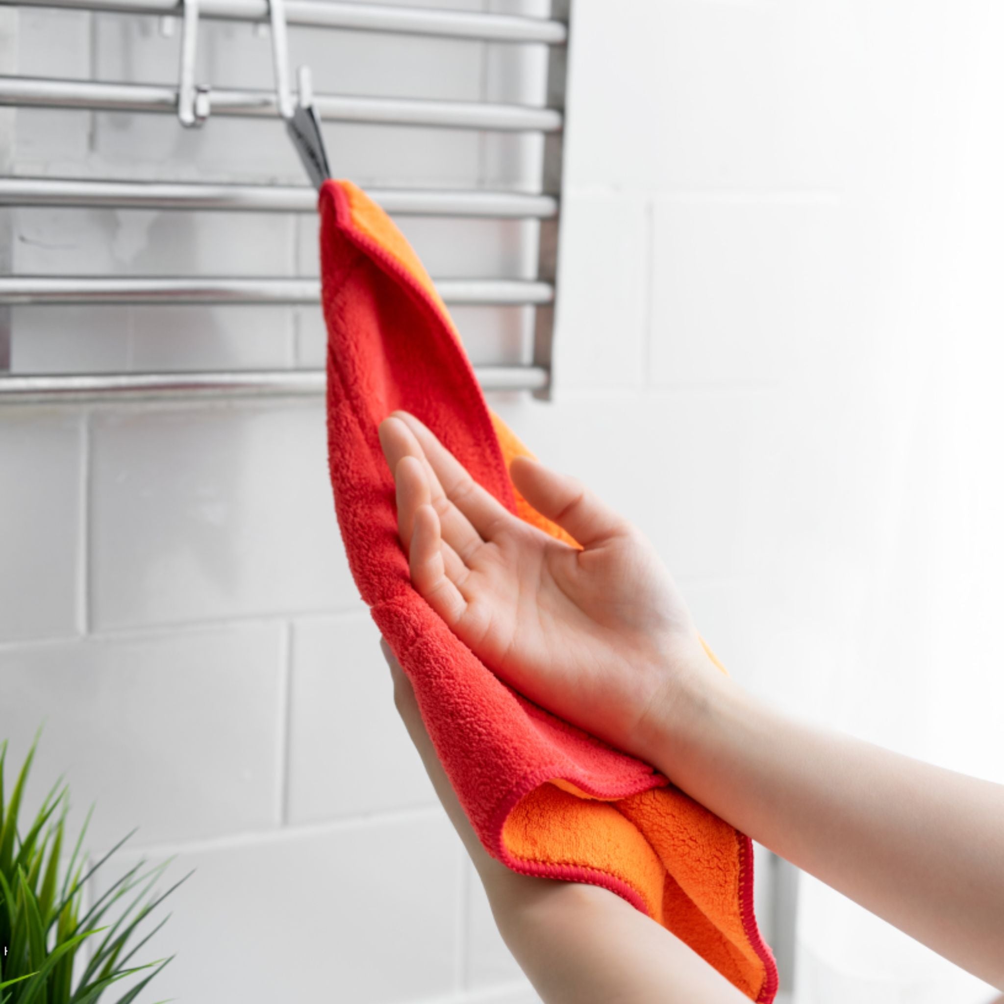 Hand wischt rote und orangefarbene Microfasertuch an Edelstahlgitterwand.