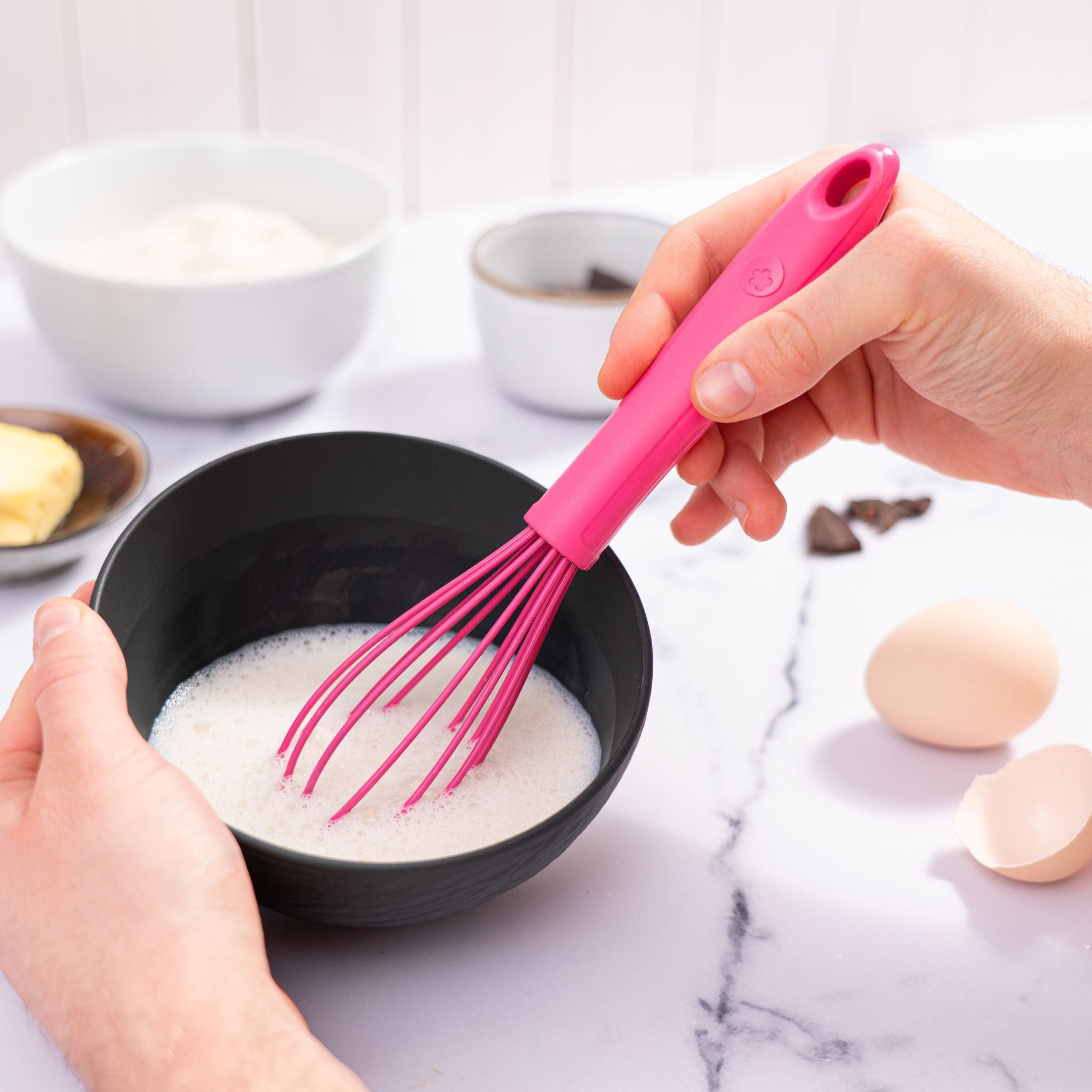 Anthrazitfarbener Schneebesen mit weichem Griff in pink, verwendet zum Mixen in schwarzer Schüssel.