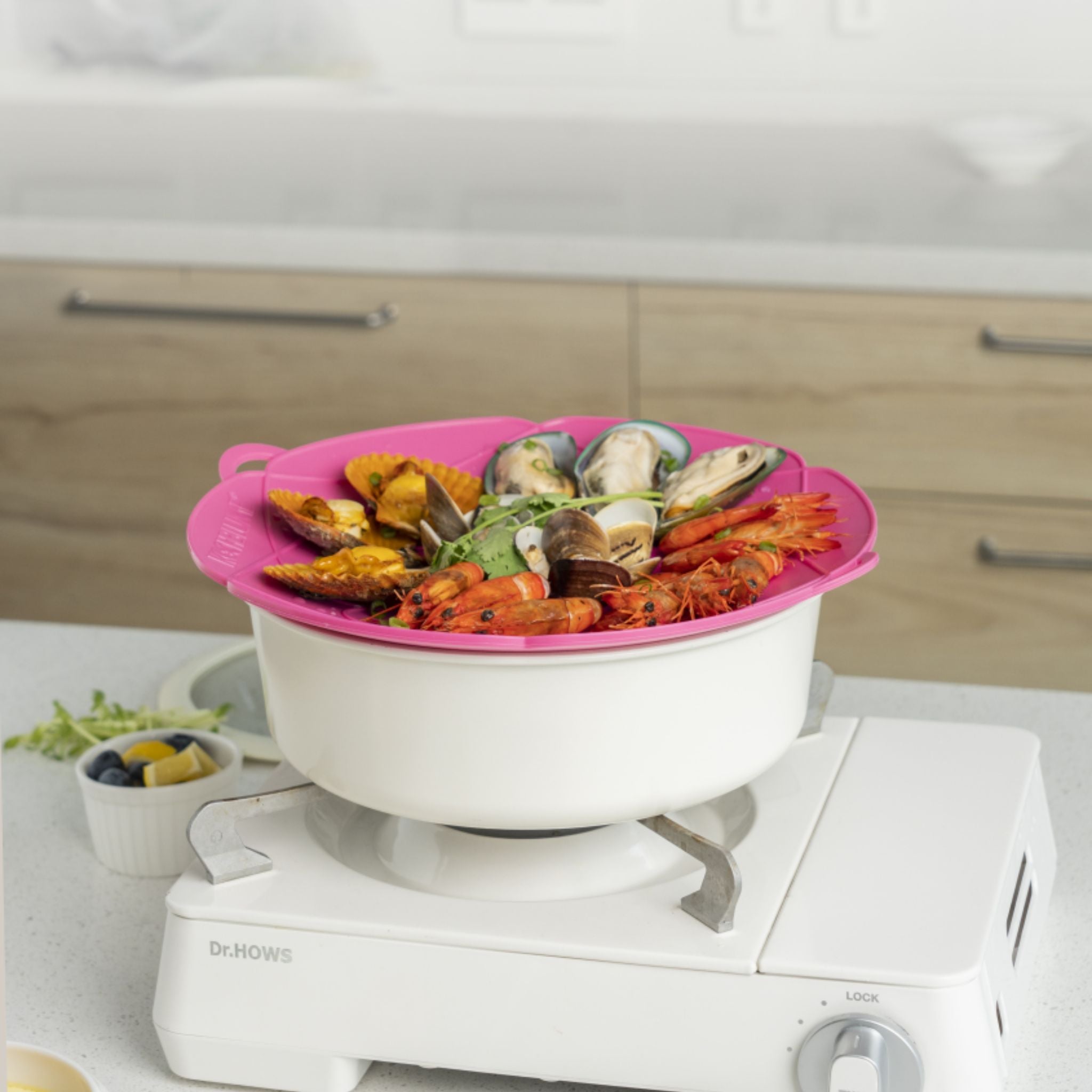 Weißer Kochtopf mit rosa Silikondeckel und Meeresfrüchten als Inhalt auf Gasherd.