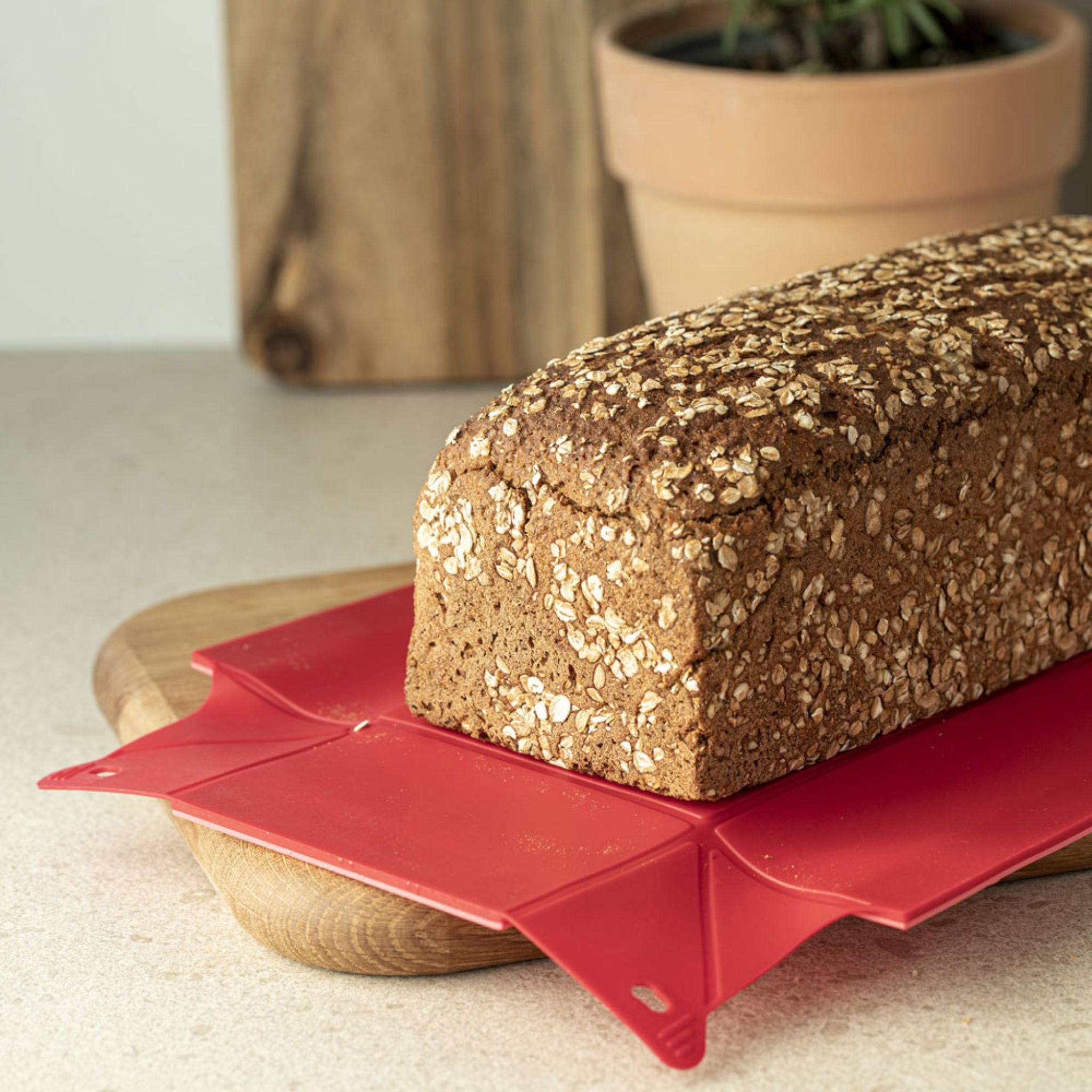 Rote Silikonbackmatte mit rutschfestem Rand, darauf ein Vollkornbrot auf Holzbrett.