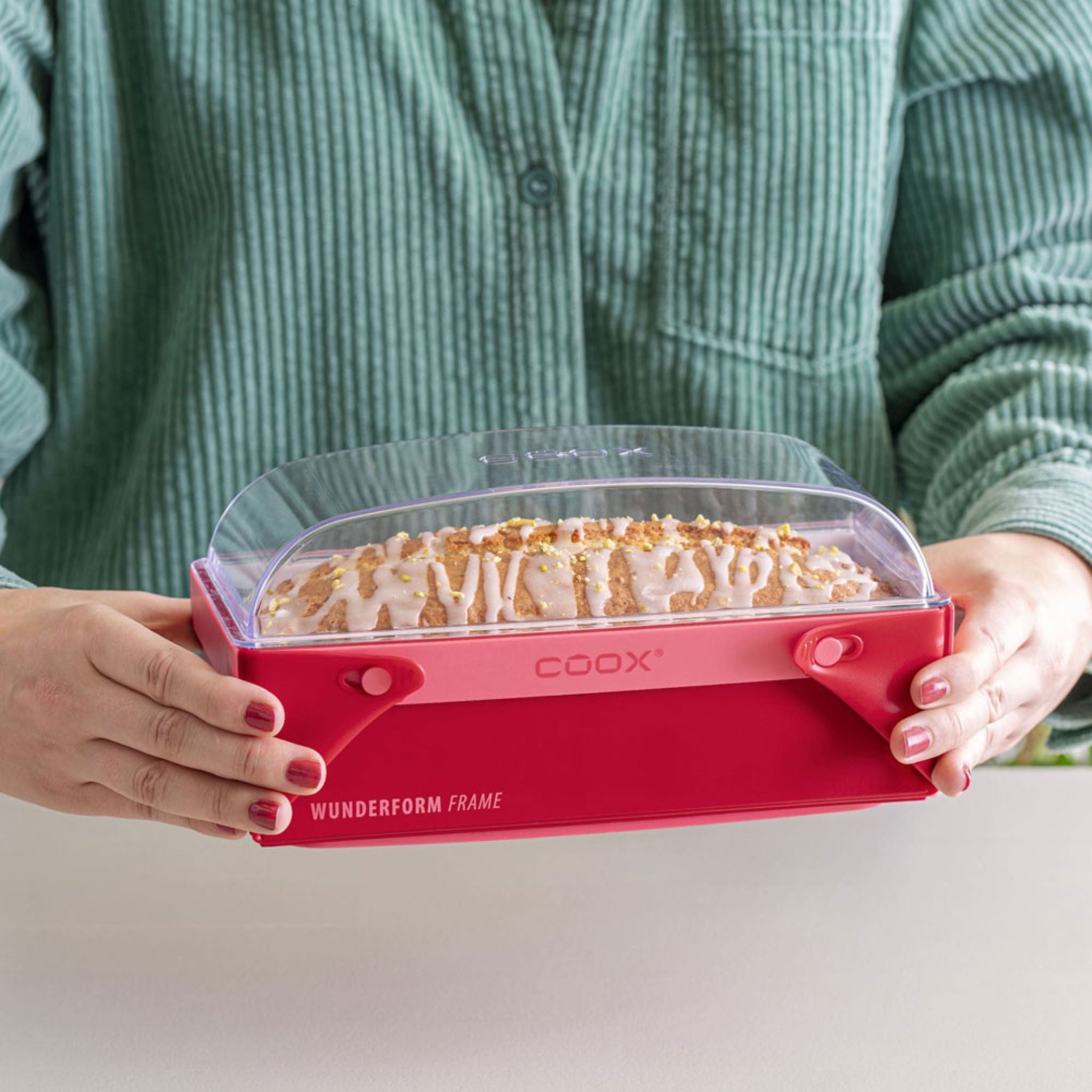 Transparenter Coox-Wunderform M Deckel mit rotem Griff, auf einer Backform mit Teig festgehalten.