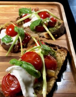 Bruschetta mit Burrata und Pesto mit Basilikum dekoriert und auf einem Tablett serviert.