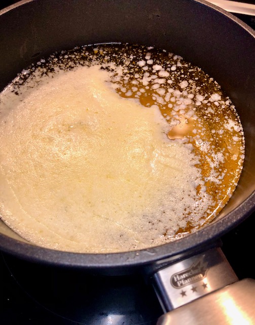 Ghee in einem Kochtopf bei der Zubereitung wie sich die Milchstoffe von der Butter trennen.