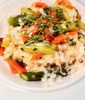 Risotto mit frischem grünem Spargel und Kartoffeln dekorativ auf einem weißen Teller angerichtet.