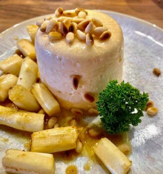 Panna Cotta mit weißem Spargel und gerösteten Pinienkernen auf einem dekorativen Teller angerichtet.