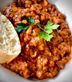 Chili con Crane mit etwas frischem Baguette auf einem Teller serviert.