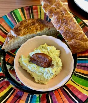 Dip aus Datteln und Curry in einer Schale auf buntem Teller mit selbstgemachtem Ciabatta-Brot serviert.