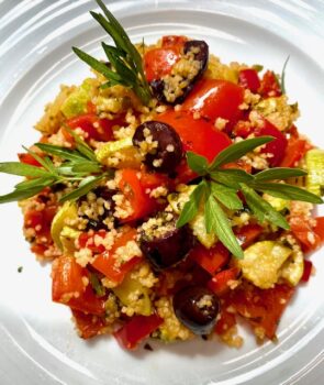 Bunte Gemüsepfanne mit Couscous auf einem weisen Teller angerichtet und etwas frischer Petersilie serviert.