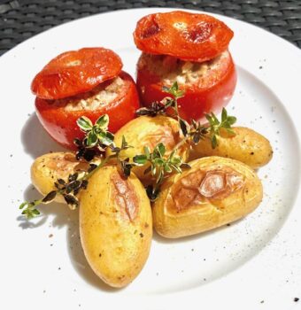 Gefüllte Ofen-Tomaten mit Hackfleisch und kleinen frischen Kartoffeln auf einem weißen Teller serviert und mit Pfeffer dekoriert.