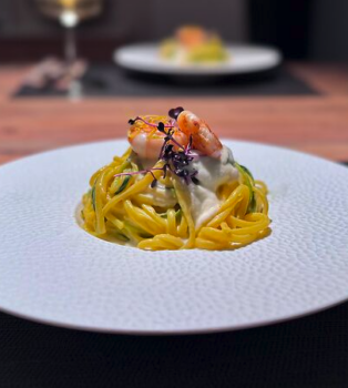 Linguine mit leckerer Zitrone-Zucchini-Sauce und einer gebratenen Garnele auf weisem Teller angerichtet.