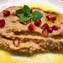 Baba Gannuş auf einem hellen Teller mit Olivenöl angerichtet und mit Granatapfel garniert.