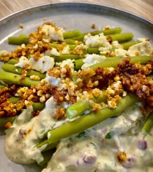 Bohnensalat mit Feta-Joghurtdip und gerösteten Semmelbrösel mit Mandeln als Topping auf einem Teller angerichtet.