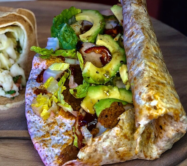 Ein Wrap (Dürüm) mit Avocado und Salat belegt auf einem Holzbrett halbtaufgewickelt.