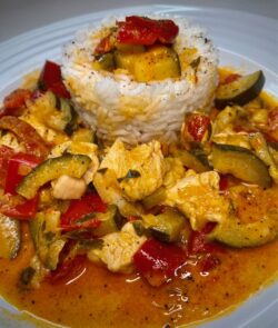 Hühnchen Curry mit Paprika und Zucchini, dazu Reis als Beilage serviert.