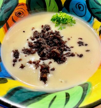 Eine Kartoffel-Kokossuppe mit Pumpernickel-Cruch auf einem bunten Teller angerichtet.