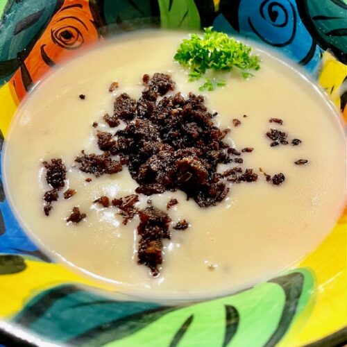 Eine Kartoffel-Kokossuppe mit Pumpernickel-Cruch auf einem bunten Teller angerichtet.