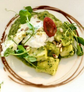 Kartoffelgnocchi mit grünem Pesto, Burrata, Pinienkerne und Kresse auf einem weißen Teller angerichtet.