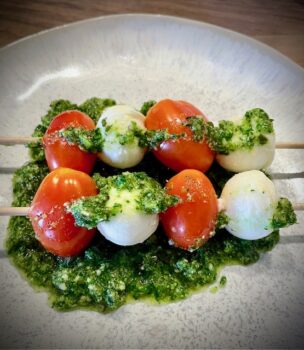 Petersilien-Erdnuss-Pesto auf einem Teller angerichtet mit Mozzarella-Tomaten-Spießchen.