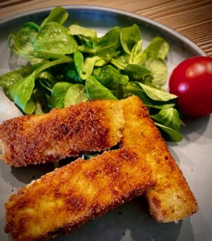 Drei panierte Tofu Stücke mit Blattsalat auf einem Teller angerichtet.