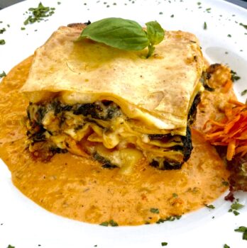 Lasagne mit Spinat und Garnelen auf einem Teller mit extra Soße angerichtet