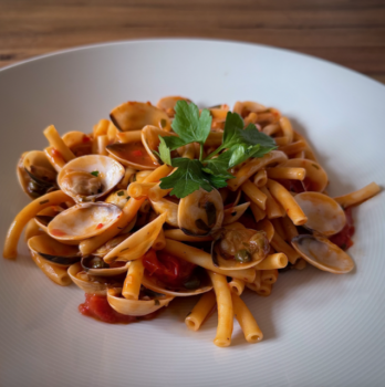 Pasta mit Venusmuscheln in roter Sauce auf weißem Teller serviert.