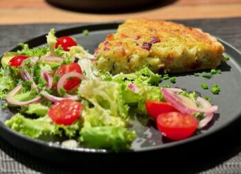 Quiche Lorraine mit frischem Salat auf einem dekorativen Teller serviert.