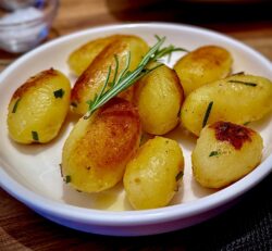 Eine weiße Schüssel mit Kartoffeln und Rosmarinzweigen, serviert als Beilage.