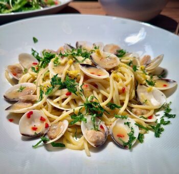 Spaghetti vongole auf einem weißen Teller mit Petersilie angerichtet und garniert.