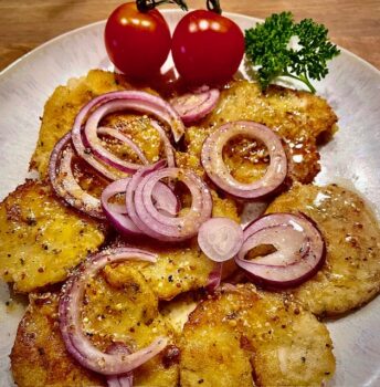 Knusprige Essigknödel mit Zwiebeln und zwei Tomaten auf einem ansprechend angerichteten Teller.