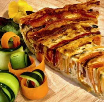 Ein Stück saftig schmeckender Gemüse Quiche mit knackigem Gemüse auf einer Holzplatte garniert.