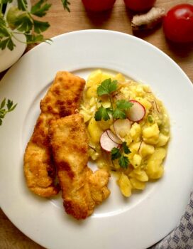 Hähnchenschnitzel mit Kartoffelsalat auf einem weißen Teller serviert.