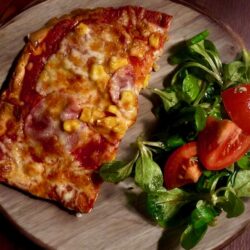 Low Carb Pizzaboden mit Salami und Mais belegt dazu ein frischer Salat als Beilage.