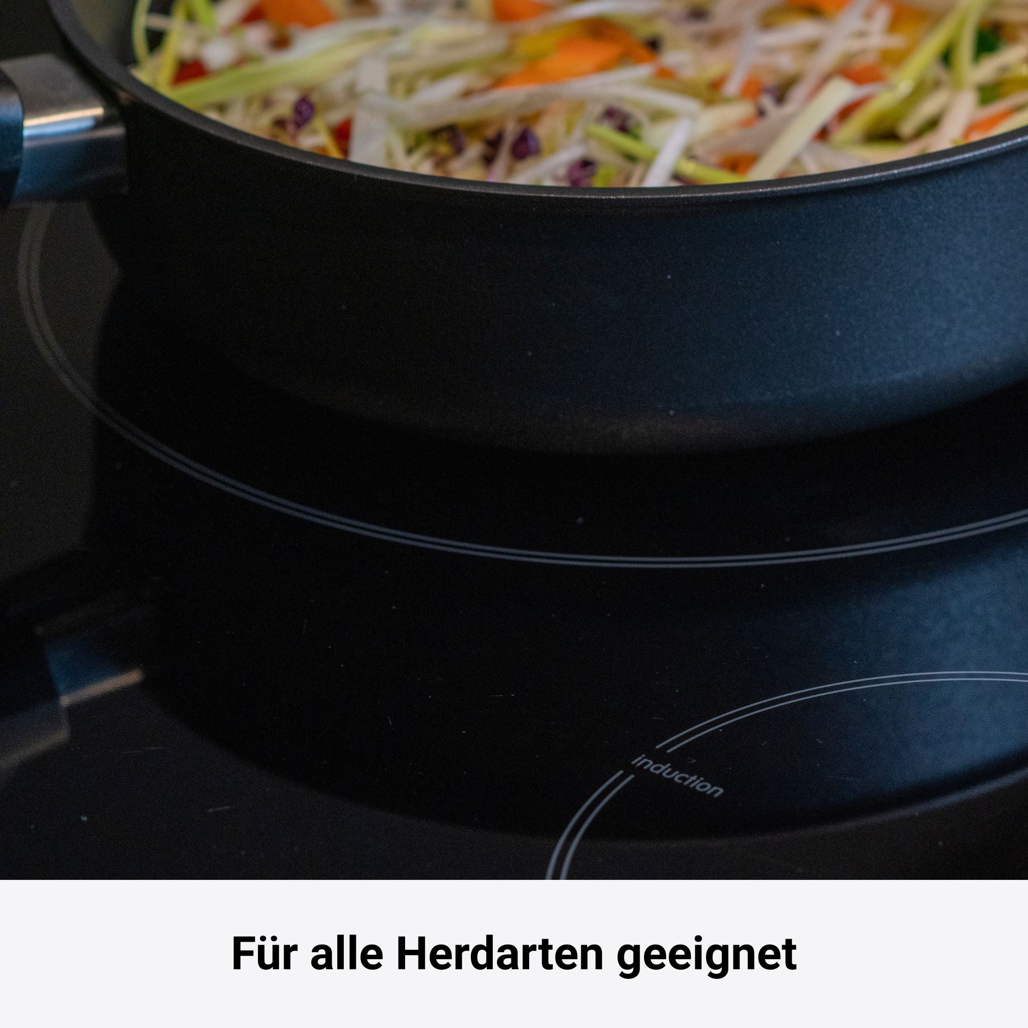 Schwarze Bratpfanne mit flachem Rand auf Ceranfeld mit buntem Gemüse darin.