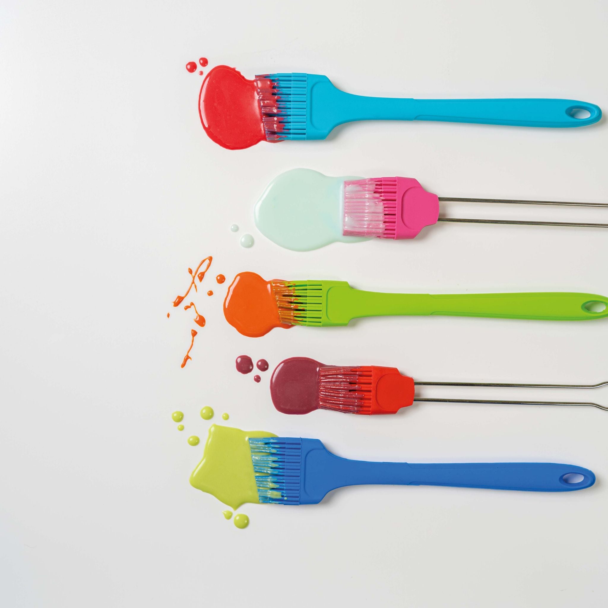 Backpinsel mit langem Griff in Blau, Pink, Grün, Rot und Dunkelblau, Tropfen bunter Farbe.