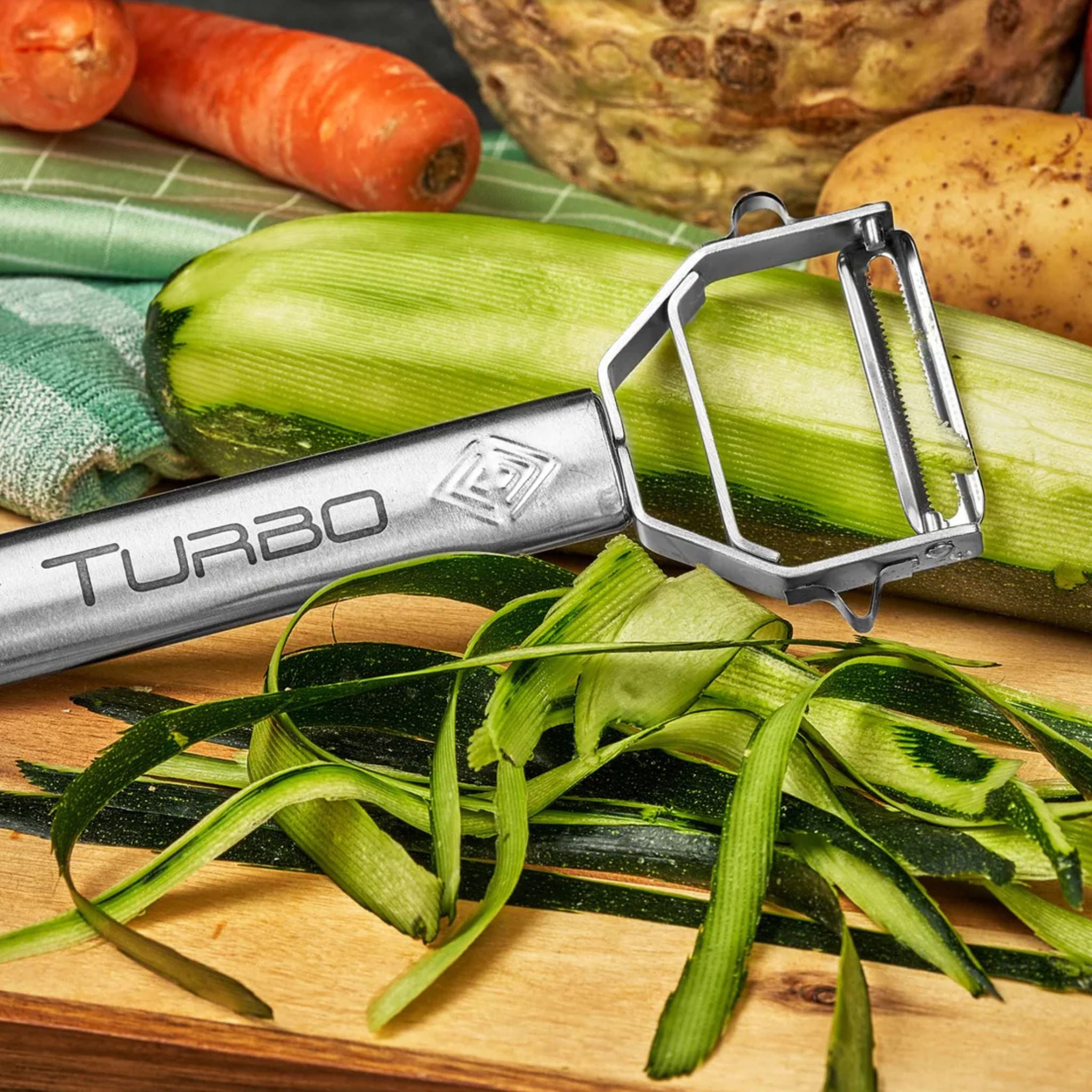 Silberner Turbo Schäler aus Edelstahl mit grünem Gemüse und Gemüseschalen auf Holzbrett.