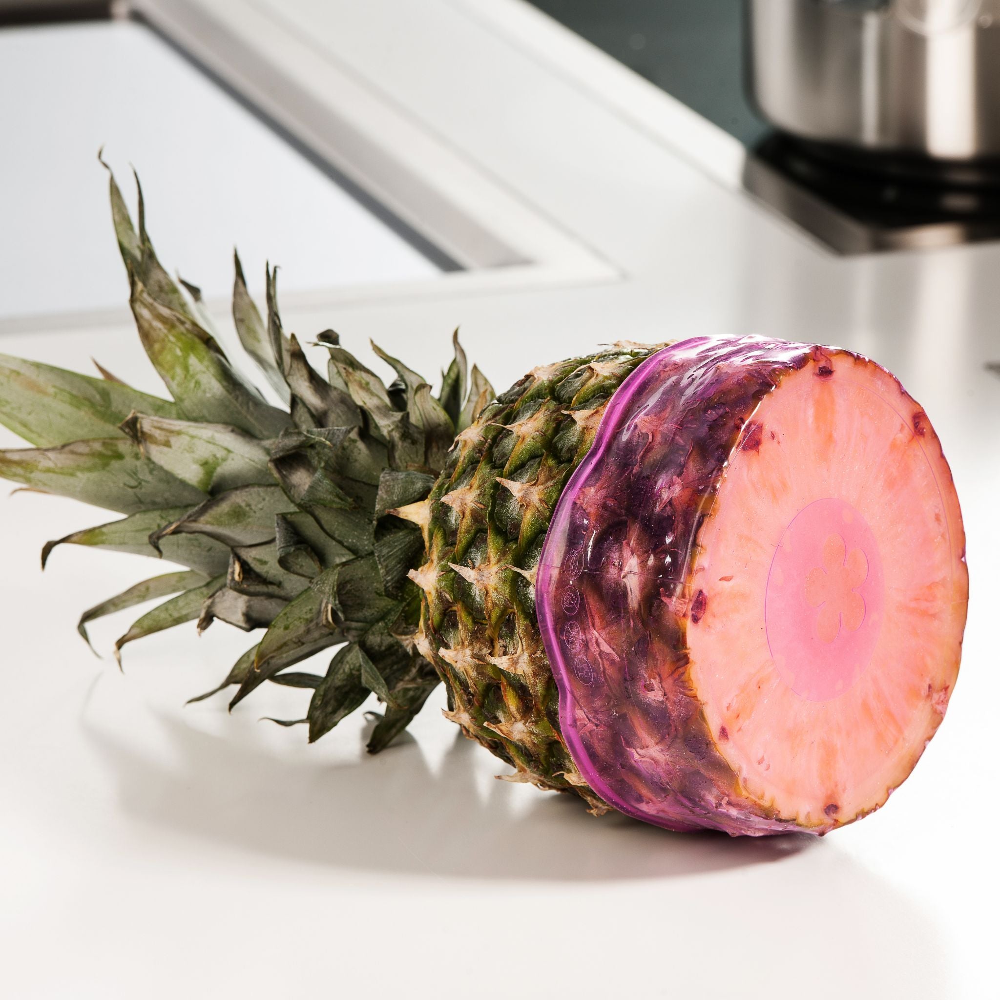 Ananas mit grünem Blatt und aufgeschnittener, violett gefärbter Schnittfläche auf weißer Fläche.