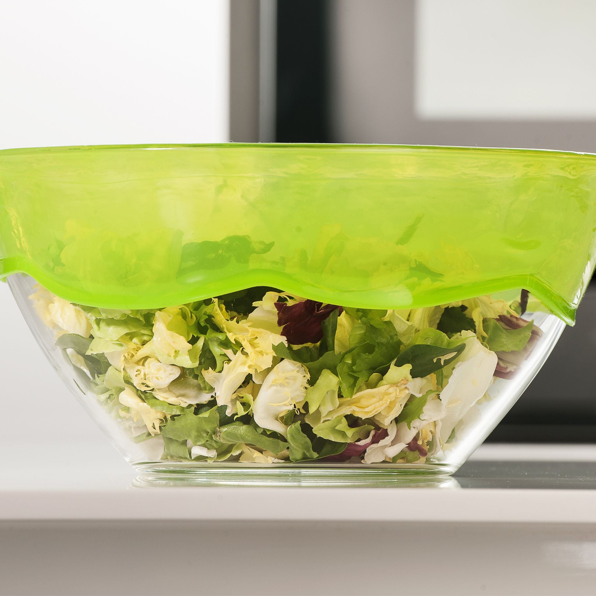 Glas-Schüssel mit grünem Stretch-Deckel, gefüllt mit gemischtem Salat.
