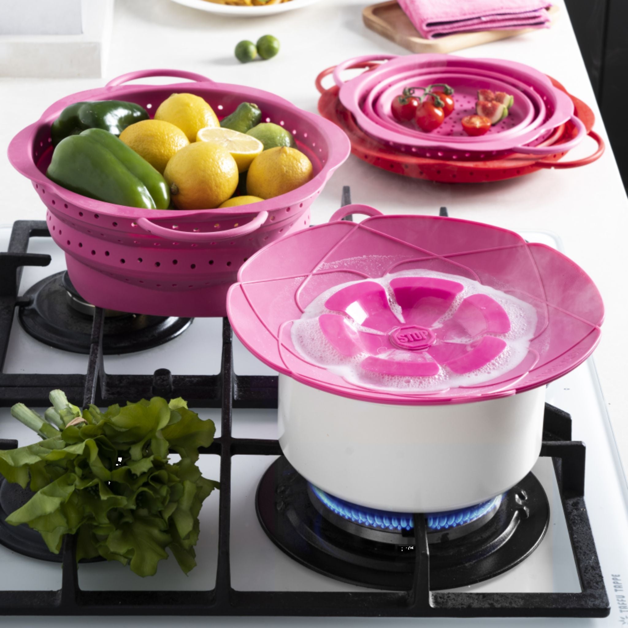 Anthrazitfarbener Dampfgarer mit pinker Kochblume als Deckel auf weißem Kochtopf über Gasflamme.