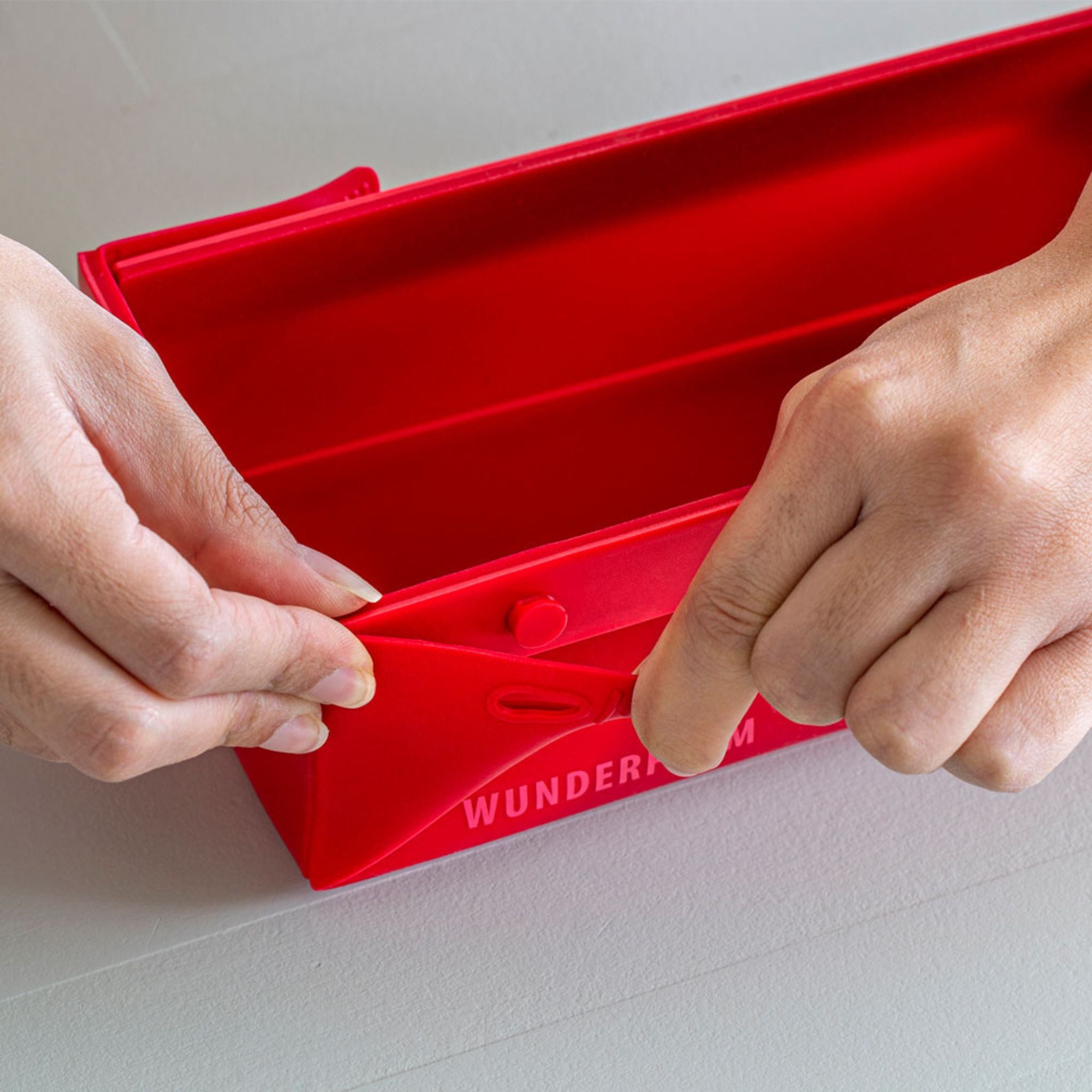 Rote flexible Silikonform mit Klappmechanismus und Gravur Wunderform, Nahaufnahme der Hände.