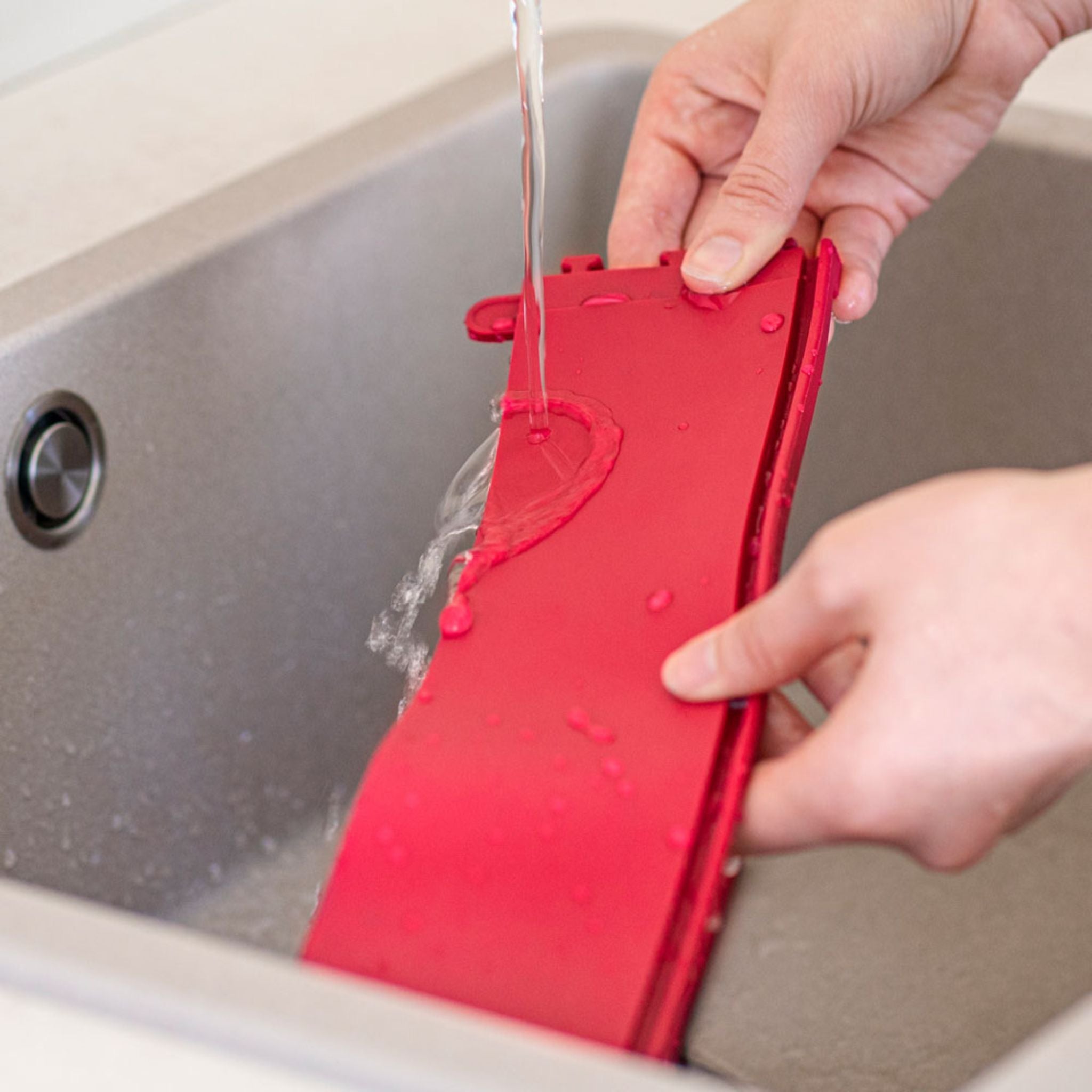 Rote flexible Backform mit Griffen wird unter fließendem Wasser abgespült.